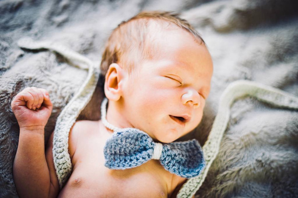 青とグレーのニット蝶ネクタイおよびズボンで寝ている生まれたばかりの赤ちゃん男の子 - 写真・画像