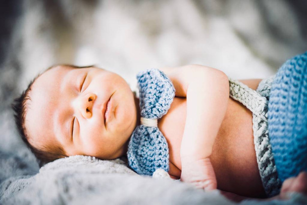 A newborn baby boy sleeping in blue and grey knitted bow tie and trousers - Foto, Imagem
