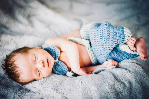 A newborn baby boy sleeping in blue and grey knitted bow tie and trousers - Photo, Image