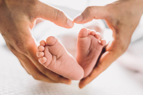 Χαριτωμένο μωρό πόδια με τις παλάμες σε σχήμα καρδιάς της μητέρας του, πάνω σε λευκό φόντο - Φωτογραφία, εικόνα