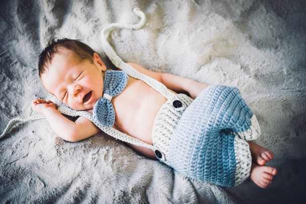 Vastasyntynyt poikavauva nukkuu sinisessä ja harmaassa neuloksessa rusetti ja housut
 - Valokuva, kuva