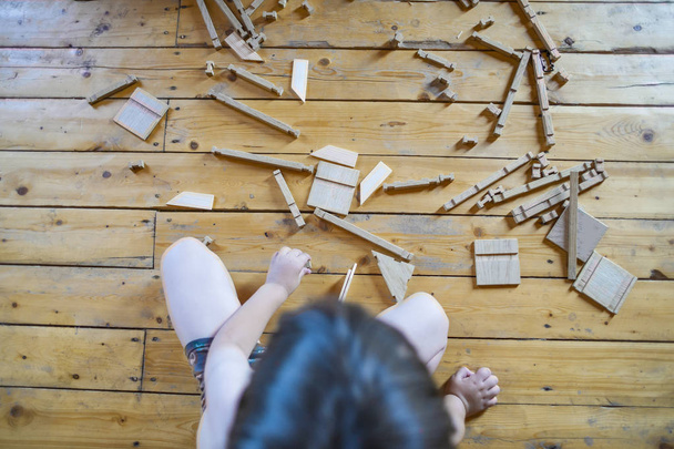 Kind, das einen umweltfreundlichen Holzdesigner spielt, der auf einem Holzboden sitzt. Entwicklung von Aufmerksamkeit und kleinlichem Stärkungsmittel bei Kindern. - Foto, Bild