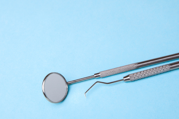 Instruments dentaires. Miroir dentaire et crochet de sonde sur fond bleu
 - Photo, image