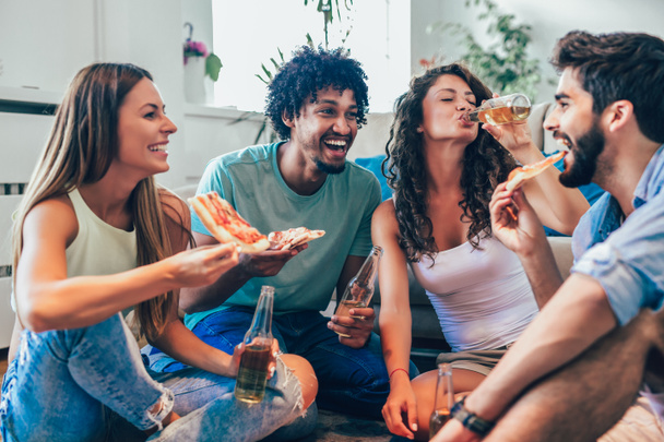 Group of young friends eating pizza and drink beer at home, home party concept  - Photo, Image
