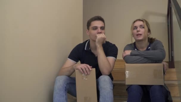 Young beautiful couple are sitting on the stairs in the house and talking - Video