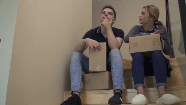 Young attractive couple are sitting on the stairs in the house and talking - Filmagem, Vídeo