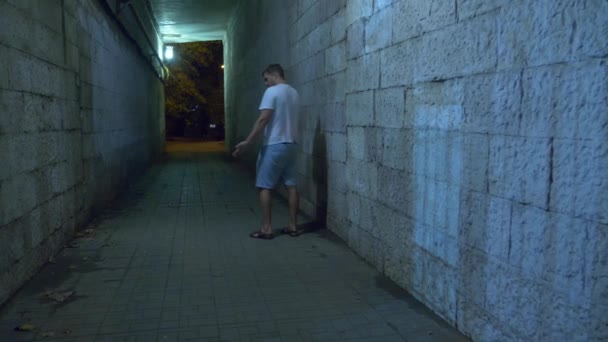 Een dronken man loopt alleen 's nachts via een voetgangerstunnel. 4k. - Video