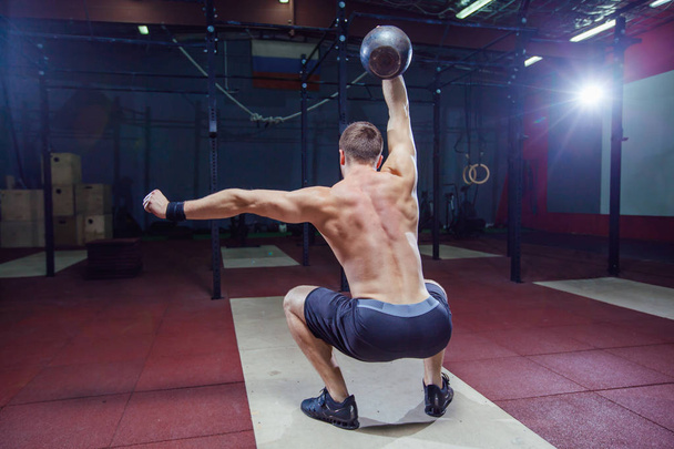 Cross training fit. Fitness man doing a weight training by lifting kettlebell. Young athlete doing kettlebell swings. Bodybuilder lifting kettlebell. Cross instructor fit at the gym. Cross in the gym - Foto, afbeelding