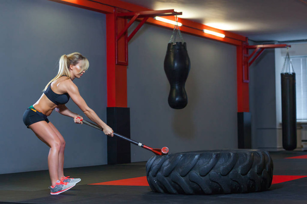 Fitness woman hitting wheel tire with hammer sledge in the gym. - Photo, Image