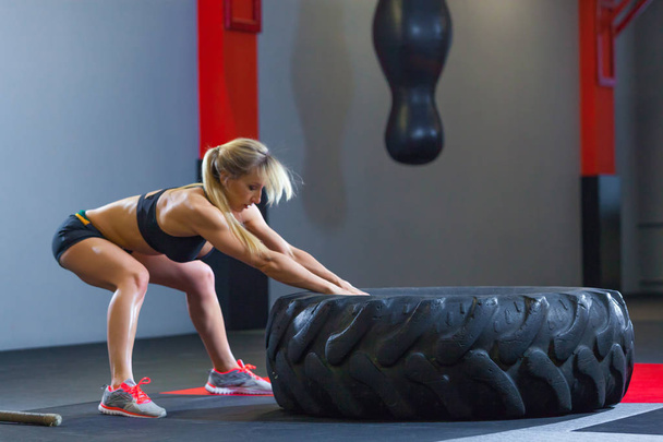 Fit female athlete working out with a huge tire, pulls in the gym. Crossfit woman exercising with big tire - Photo, image