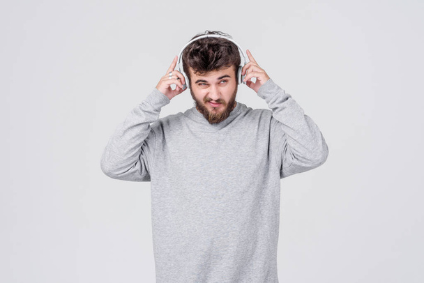 Genç bir adam rahat kıyafetler içinde sakallı kablosuz kulaklık hoş müzik dinler. Metin için yer ile gri arka plan - Fotoğraf, Görsel