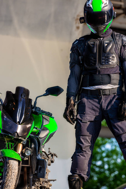 мотоциклист в шлеме и в защитном костюме стоит под мостом
 - Фото, изображение