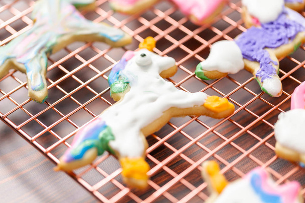 Galletas de azúcar en forma de unicornio decoradas por niños con glaseado real en estante de secado
. - Foto, imagen