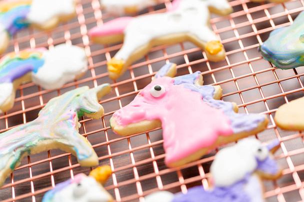 Galletas de azúcar en forma de unicornio decoradas por niños con glaseado real en estante de secado
. - Foto, imagen