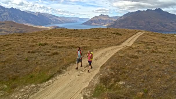 Aerial drone of active healthy Caucasian male and female trekking on natural road of The Remarkables Lake Wakatipu Nueva Zelanda
 - Metraje, vídeo