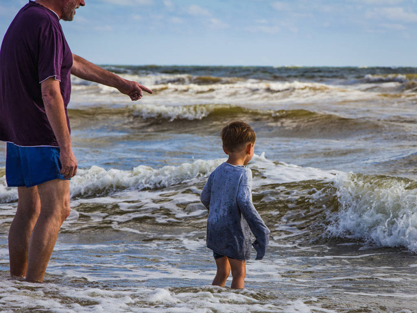 Допитливий малюк в мокрий одяг ознайомитися з дідусем морські хвилі. Північне море, шторм, ранок. - Фото, зображення