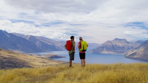 Jonge Kaukasische adventure mannelijke en vrouwelijke wandelaars met rugzakken genieten van wandelen in de natuur van The Remarkables Nieuw-Zeeland  - Video