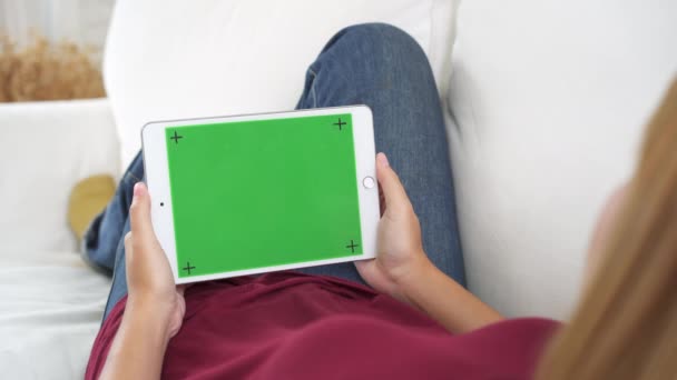 Genç Asyalı kadın ile yeşil ekran siyah tablet cihaz kullanarak. Oturma odasında kanepede otururken sayfalarını kaydırma Asyalı kadın tablet, holding. Chroma anahtar. - Video, Çekim