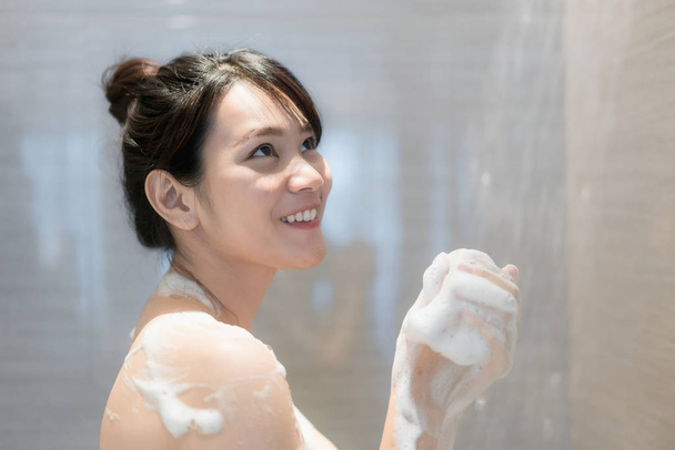 Jeune femme asiatique prenant une douche dans la salle de bain avec pomme de douche. Vous avez l'air heureux et relax
. - Photo, image