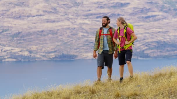 Gelukkig Kaukasische mannelijke en vrouwelijke reizigers met rugzakken op hun wandel avontuur expeditie Lake Wakatipu Nieuw-Zeeland  - Video