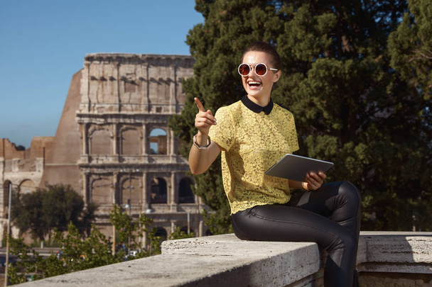 mujer turista de moda feliz en blusa amarilla con tableta PC señalando a un lado cerca del Coliseo, Roma, Italia
 - Foto, imagen