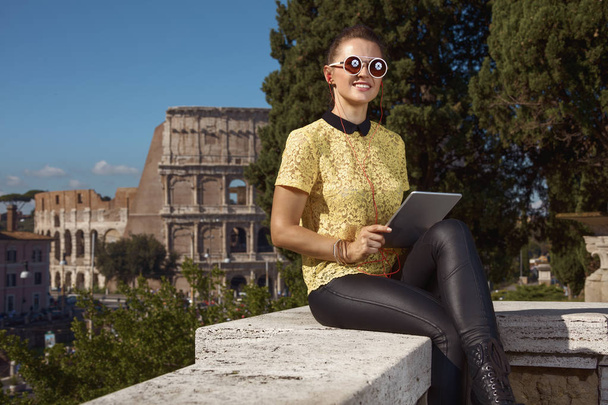 smiling young woman in yellow blouse having audio excursion on tablet PC near Colosseum , Rome, Italy - 写真・画像