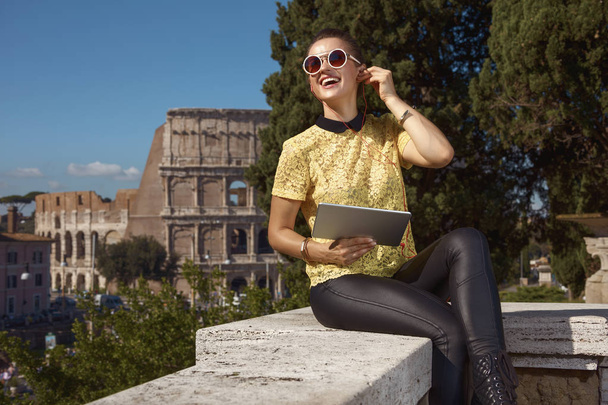 back view of tourist woman sitting on parapet and listening to audio guide on tablet PC near Colosseum , Rome, Italy  - Photo, Image