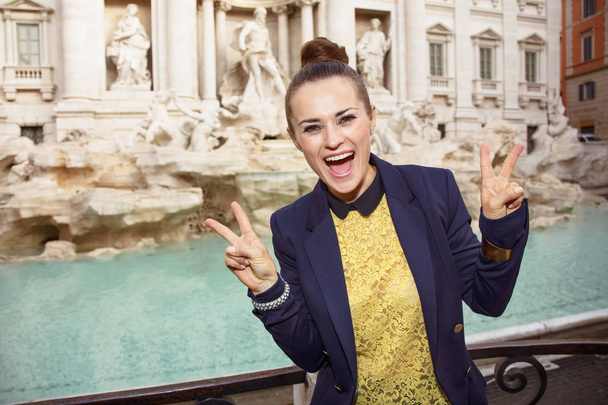 happy modern woman in yellow blouse and blue jacket showing victory gesture near Trevi Fountain, Rome, Italy - Foto, Imagen