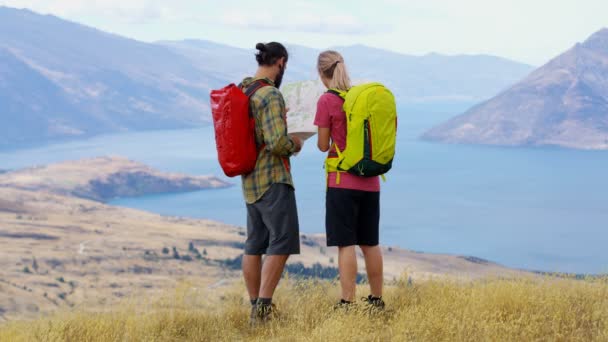 若い白人の冒険旅行ハイキングやリマーカブルズ湖ワカティプ新しいニュージーランドの地図を読んでのツアーを計画  - 映像、動画