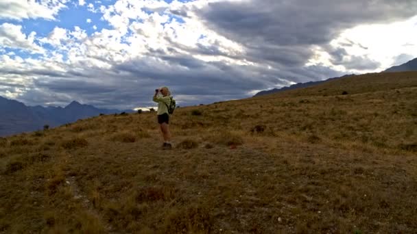 Dron aéreo de la mujer caucásica retirada en forma con prismáticos disfrutando de trekking de The Remarkables Lake Wakatipu Nueva Zelanda
 - Metraje, vídeo