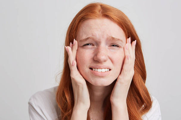 Porträt einer traurig gestressten rothaarigen jungen Frau mit langen Haaren und Sommersprossen, die ihre Schläfen berührt und vereinzelt Kopfschmerzen auf weißem Hintergrund hat - Foto, Bild