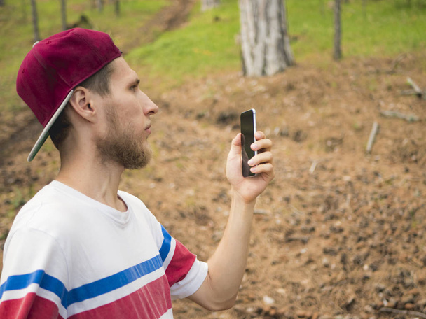 close young bearded man taking a photo with phone walking in the switzerland pine forest - Foto, imagen