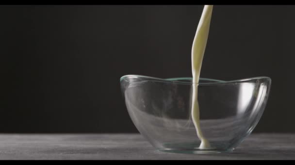 milk being poured in glass bowl, dark background , slow motion  - Felvétel, videó