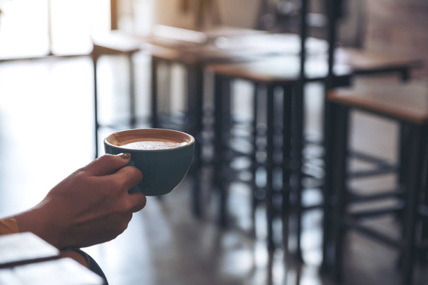 Κινηματογράφηση σε πρώτο πλάνο εικόνα ενός χεριού που κρατάει ένα φλιτζάνι καφέ στο καφέ - Φωτογραφία, εικόνα