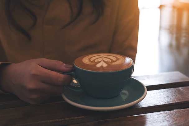 Closeup image of a woman holding a blue cup of hot coffee on table in cafe - Foto, Bild