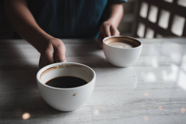 Closeup image of hands holding two white cups of hot coffee on table in cafe - Photo, image