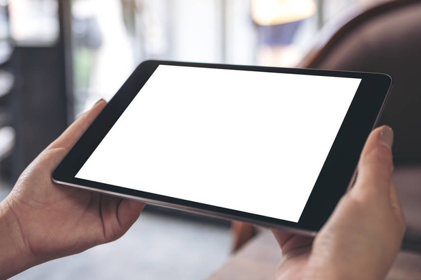 Mockup beeld van handen met zwarte tablet pc met witte leeg bureaublad scherm in café - Foto, afbeelding