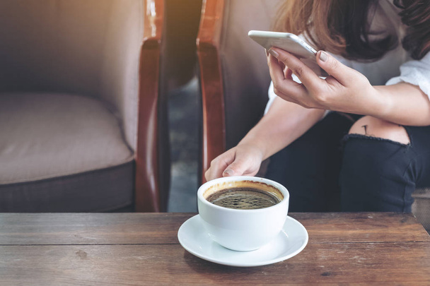 Крупним планом зображення жінки, що тримає, використовуючи і торкаючись смартфона під час пиття кави в кафе
 - Фото, зображення