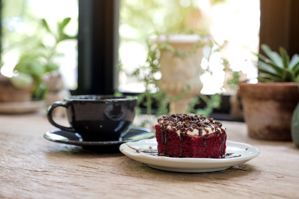 Ένα κομμάτι κόκκινο βελούδινο κέικ με φλιτζάνι καφέ στο ξύλινο τραπέζι στο καφέ - Φωτογραφία, εικόνα