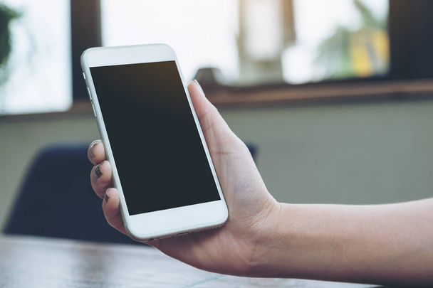 Maketa obraz ženy držící bílý mobilní telefon s prázdnou černou obrazovku na dřevěný stůl - Fotografie, Obrázek