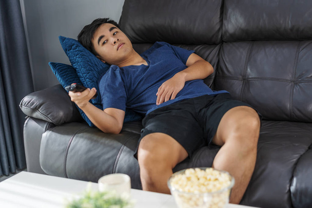 young bored man watching tv and sitting on sofa in the living room - Foto, imagen