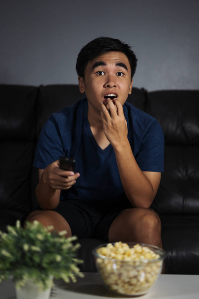 Shocked young man watching at tv and sitting on sofa in the living room at night - Foto, immagini