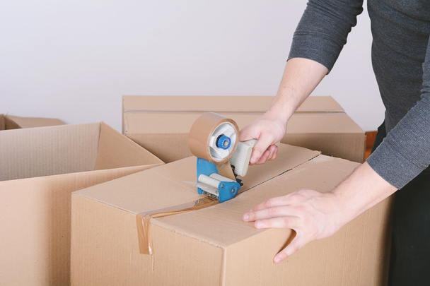 Man sealing a shipping cardboard box with tape dispenser. Indoors - Photo, Image
