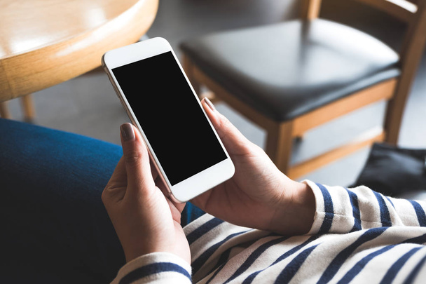 Imagem Mockup de mãos segurando telefone celular branco com tela preta em branco no café de madeira
 - Foto, Imagem