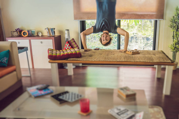 A man stands on his hands upside down in the living room. - Photo, Image