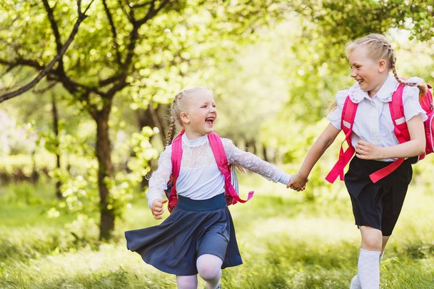 two funny school girls with school backpacks running holding hands outdoors - Foto, afbeelding
