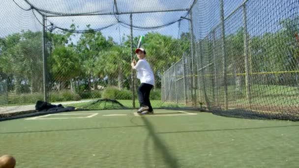 Slow motion shot of a little boy practicing baseball inside batting cages at baseball park - Footage, Video