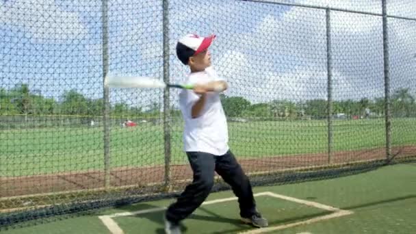 Hidasliikkeinen kuva pojasta lyömässä palloa baseball-puiston lyöntihäkeissä.
 - Materiaali, video