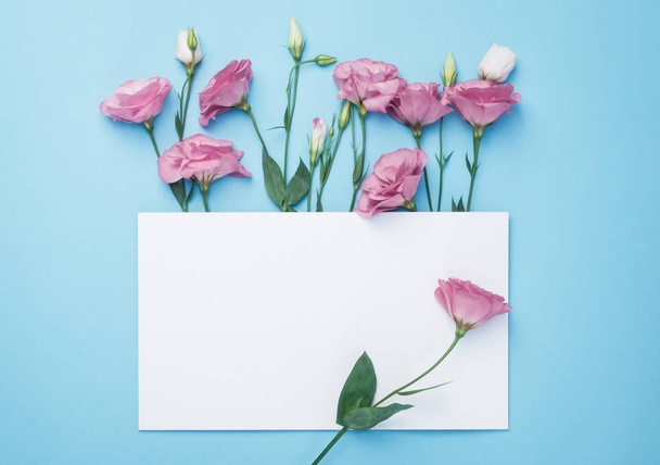Flowers composition. Wreath made of pink flowers with white paper card on blue background. Flat lay, top view, copy space - Fotó, kép