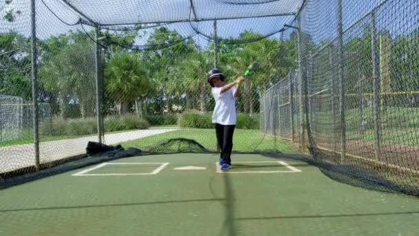 Disparo en cámara lenta de un niño balanceando su bate mientras practica dentro de jaulas de bateo de un parque de béisbol
 - Metraje, vídeo